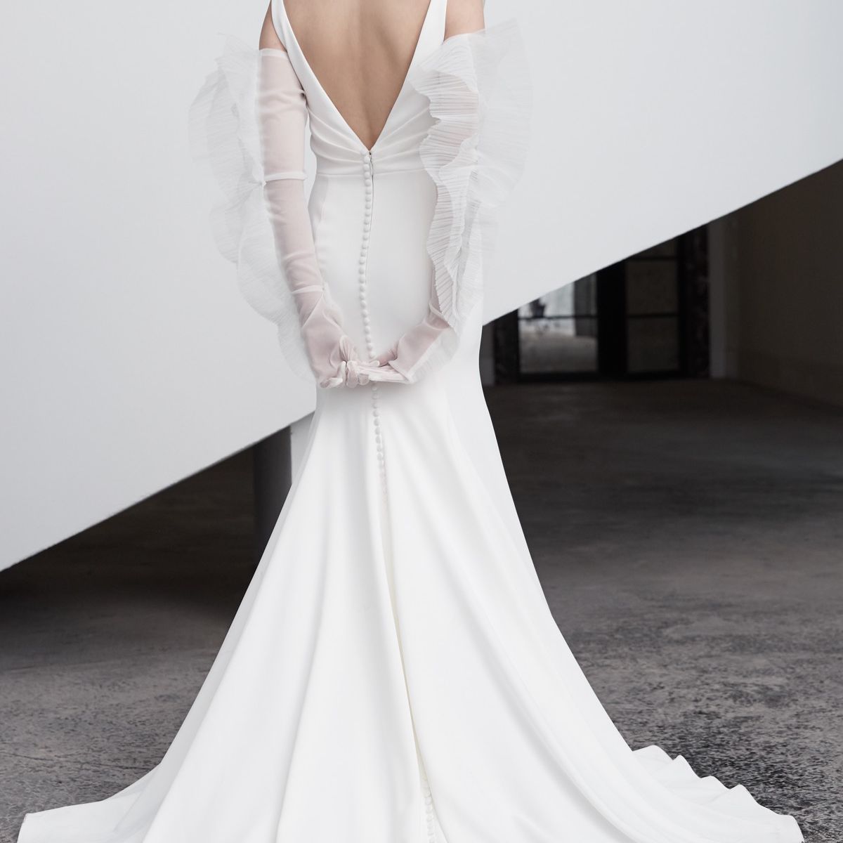 模特穿着v字背带的无袖长裙，拖着长长的裙裾，戴着一副长臂薄纱手套