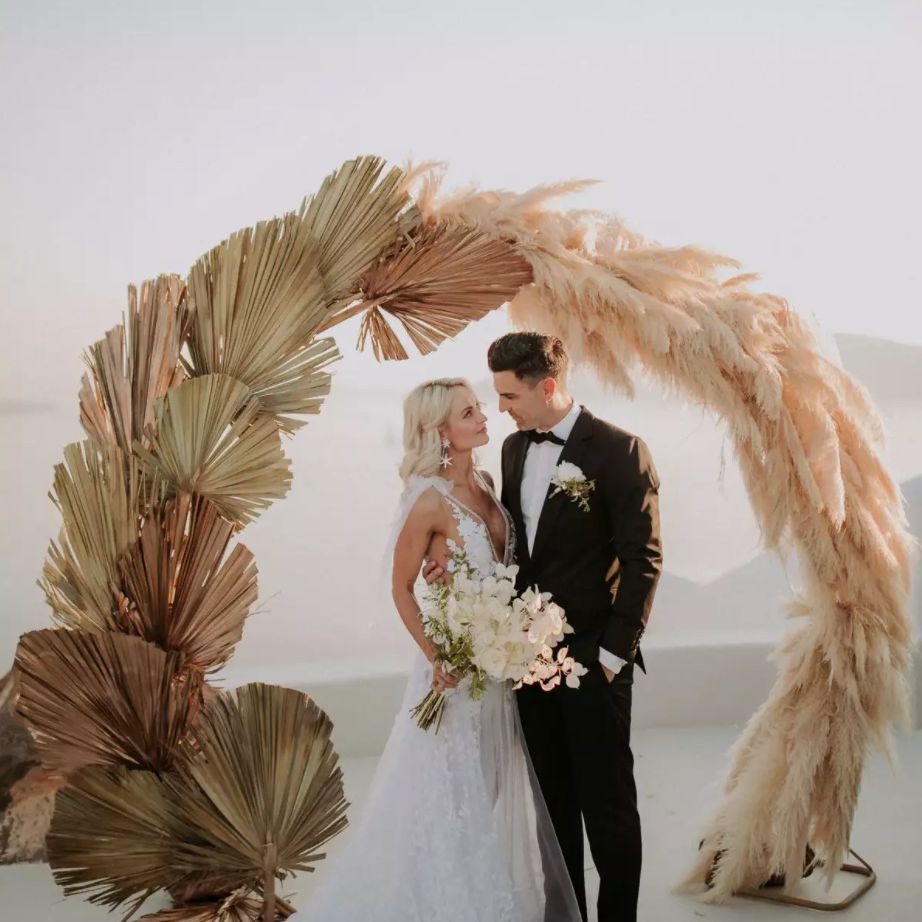 站立在干蒲苇草和棕榈叶前面的新婚夫妇在圆婚礼曲拱前面