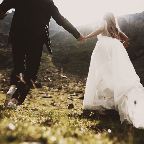 新娘新郎的手牵着手在夕阳对山跑起来“class=