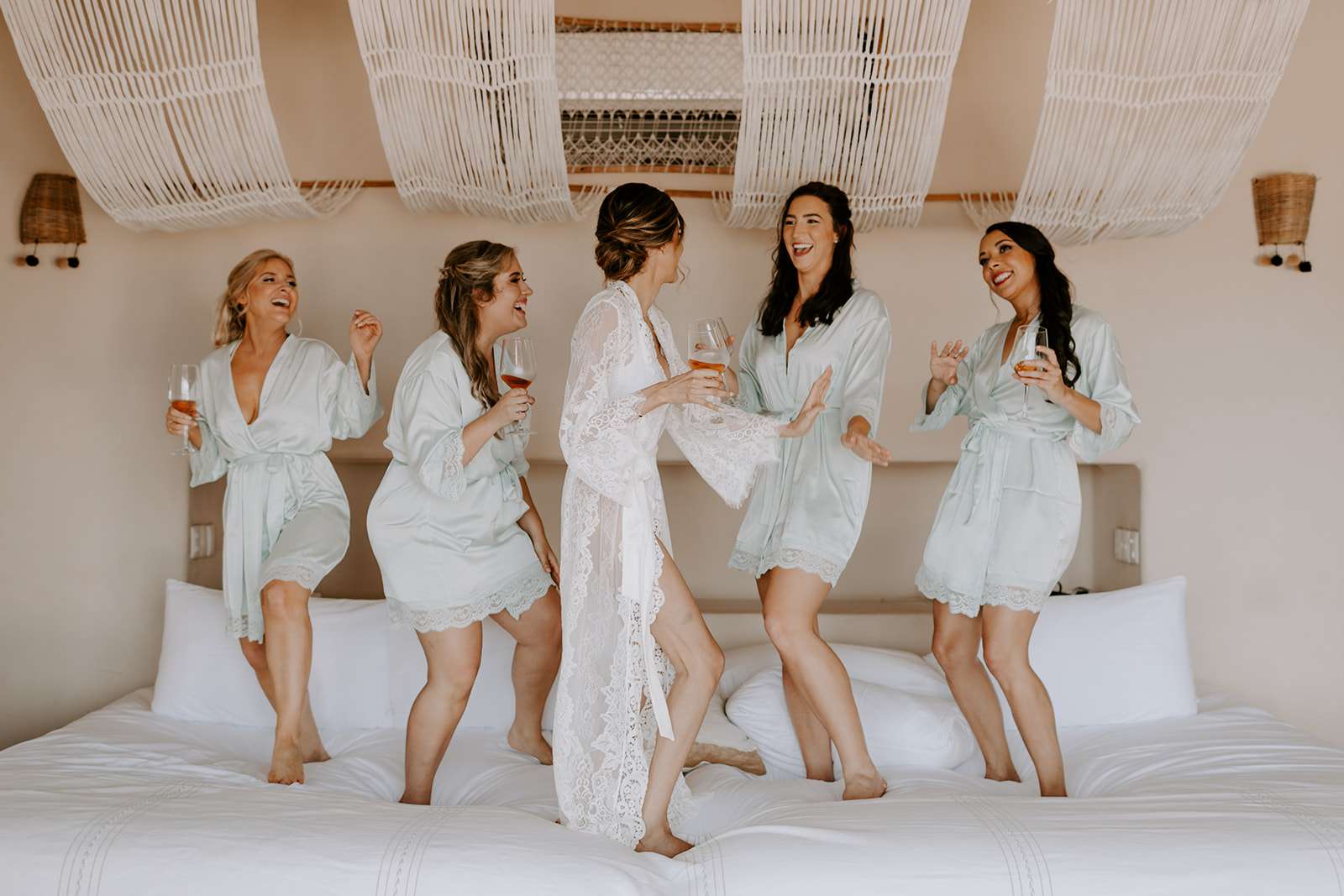 新娘和伴娘在床上跳舞，喝着鸡尾酒欢笑