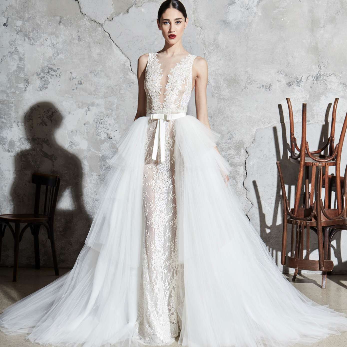 模型与幻觉floral-embroidered鞘礼服领口,一个白色的蝴蝶结腰带,和一个分层的薄纱半裙