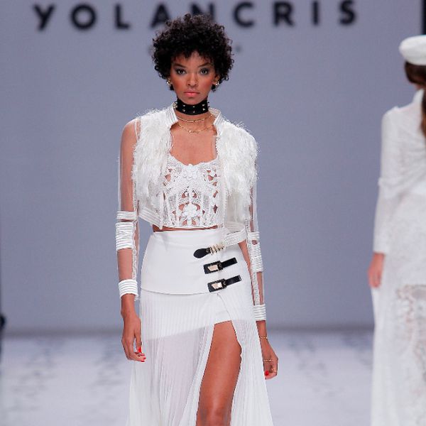 在一个紧身胸衣上面的模型，钩针绣花和3D花朵和绉纱和褶皱乔木饰品裙，侧面有一个高缝隙和黑色和金扣细节，戴着透明轰炸机带有边缘的夹克