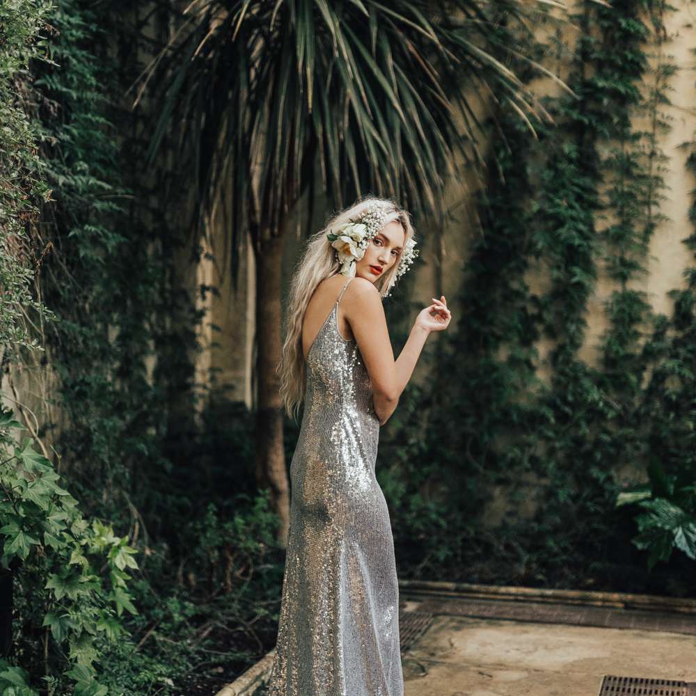 模型在一个秘密庭院里穿着与鲜花的银色婚纱礼服在她的头发