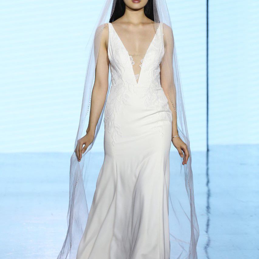 模特身着无袖婚纱，低胸领口和蕾丝贴花