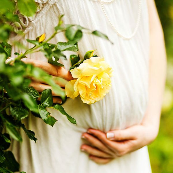 在黄玫瑰旁边抱着怀孕的肚子的女人