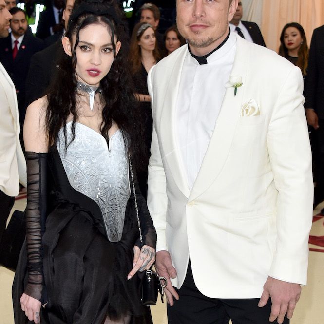 Grimes戴着一颗球形黑色假发，奶油和黑色礼服，纯粹的胳膊件，而Elon Musk在奶油和黑色的Tux旁边站在她身边。