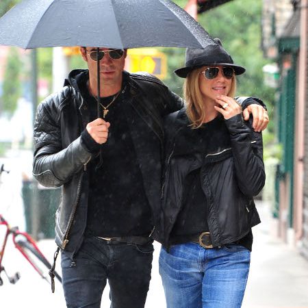 贾斯汀·塞洛克斯(左)和詹妮弗·安妮斯顿在一把黑色雨伞下散步