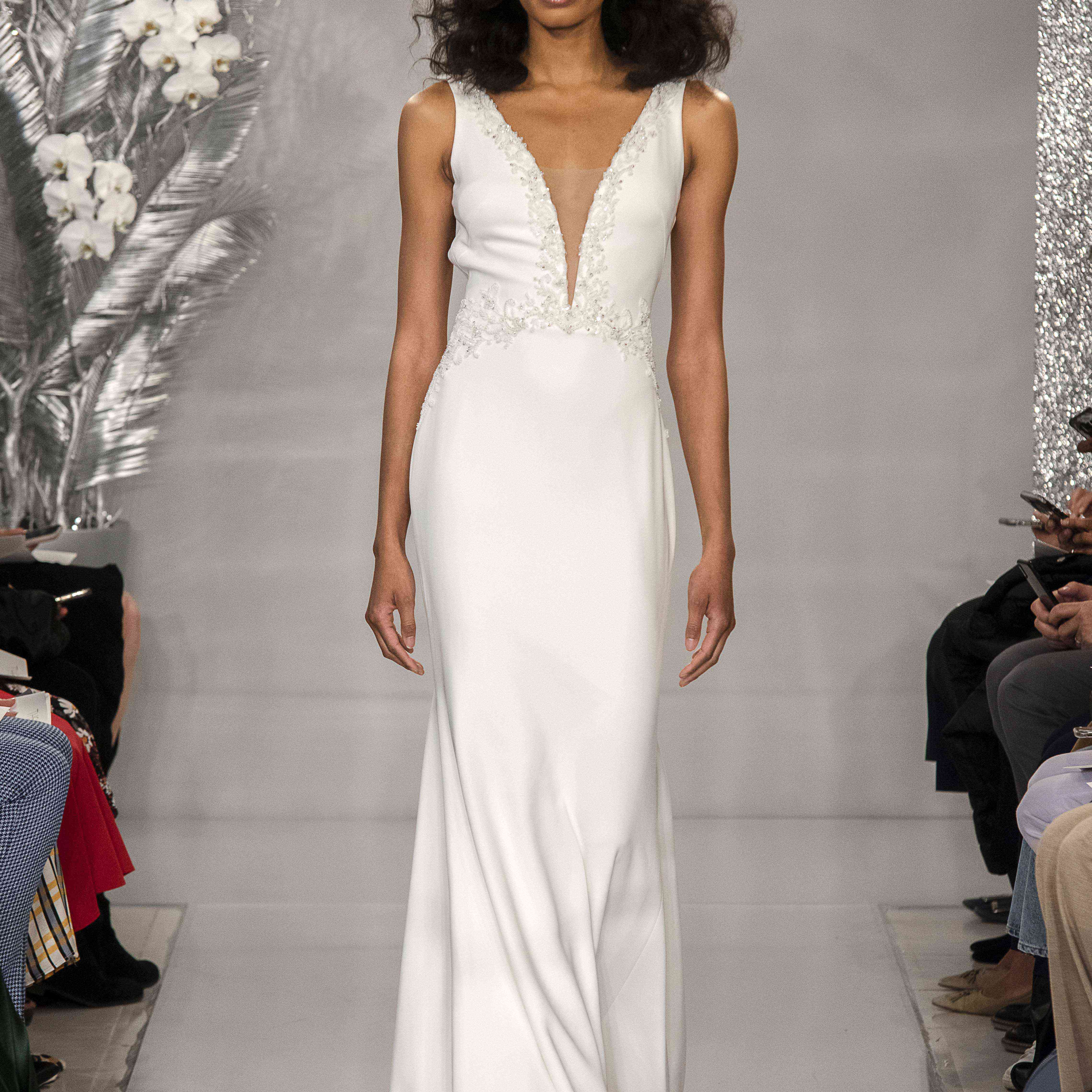 模特身穿无袖美人鱼绉纱礼服，领口深v，胸衣上点缀着珠子