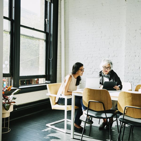 两位女士坐在桌边，看着一台笔记本电脑和平板电脑