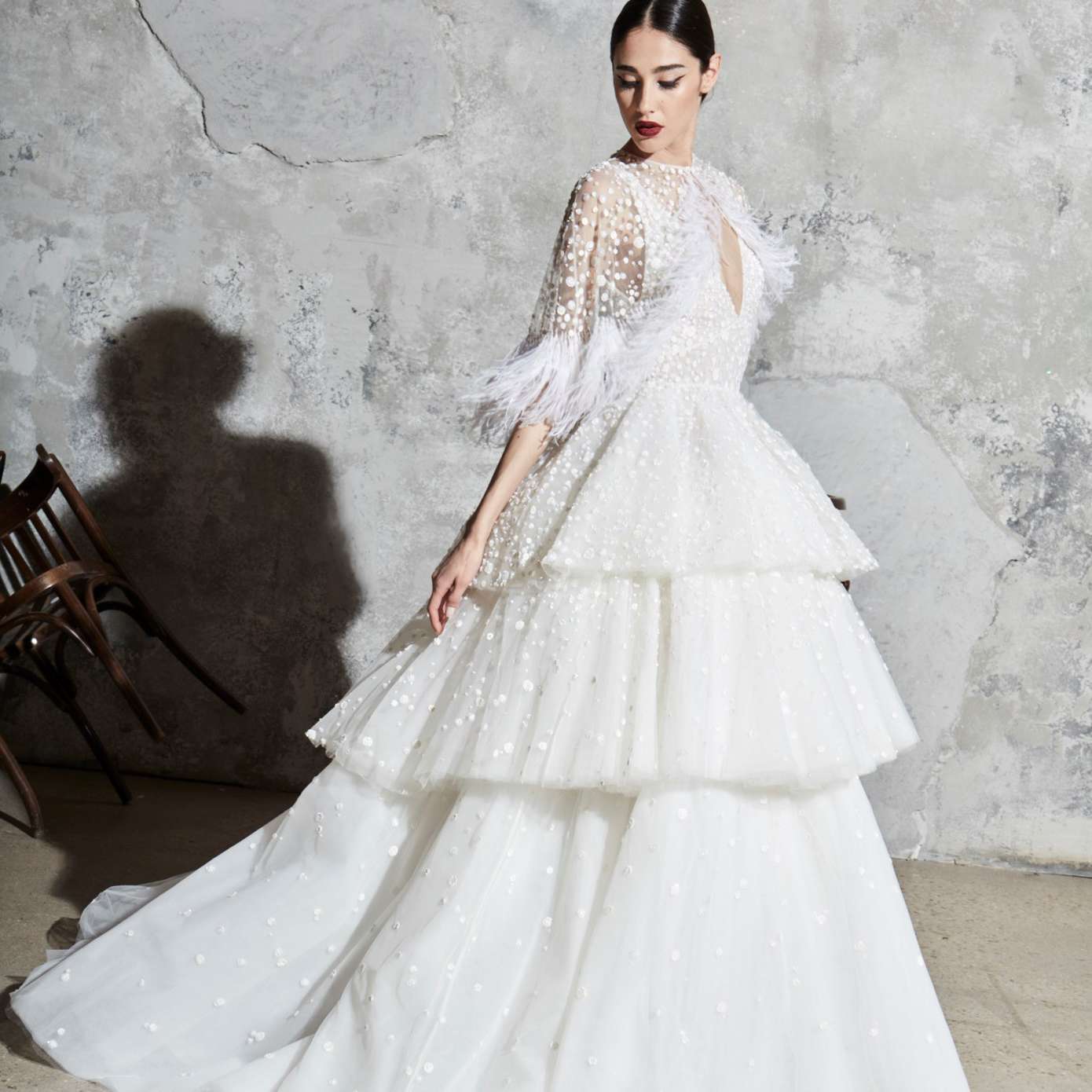 模型在v领舞会礼服有亮片和三层裙与羽毛细节进行匹配的透明薄纱耸耸肩