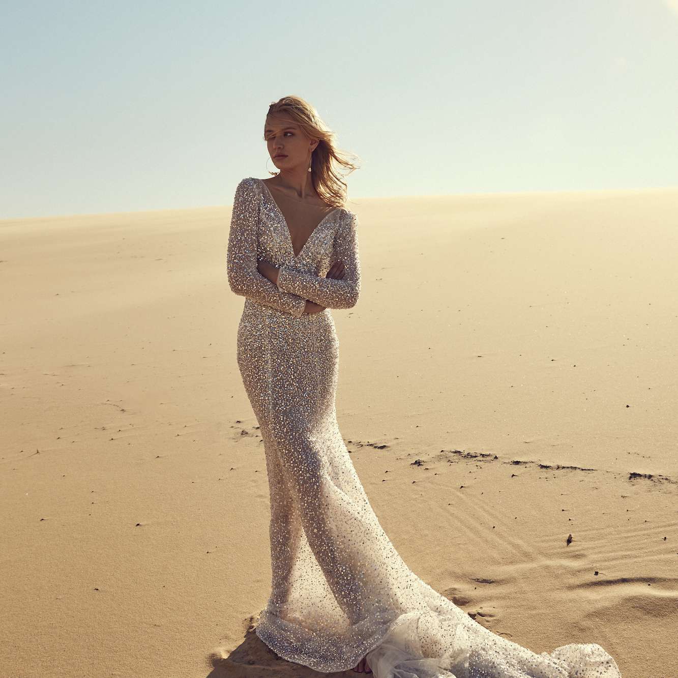 身穿银色亮片连衣裙的模特站在沙漠中