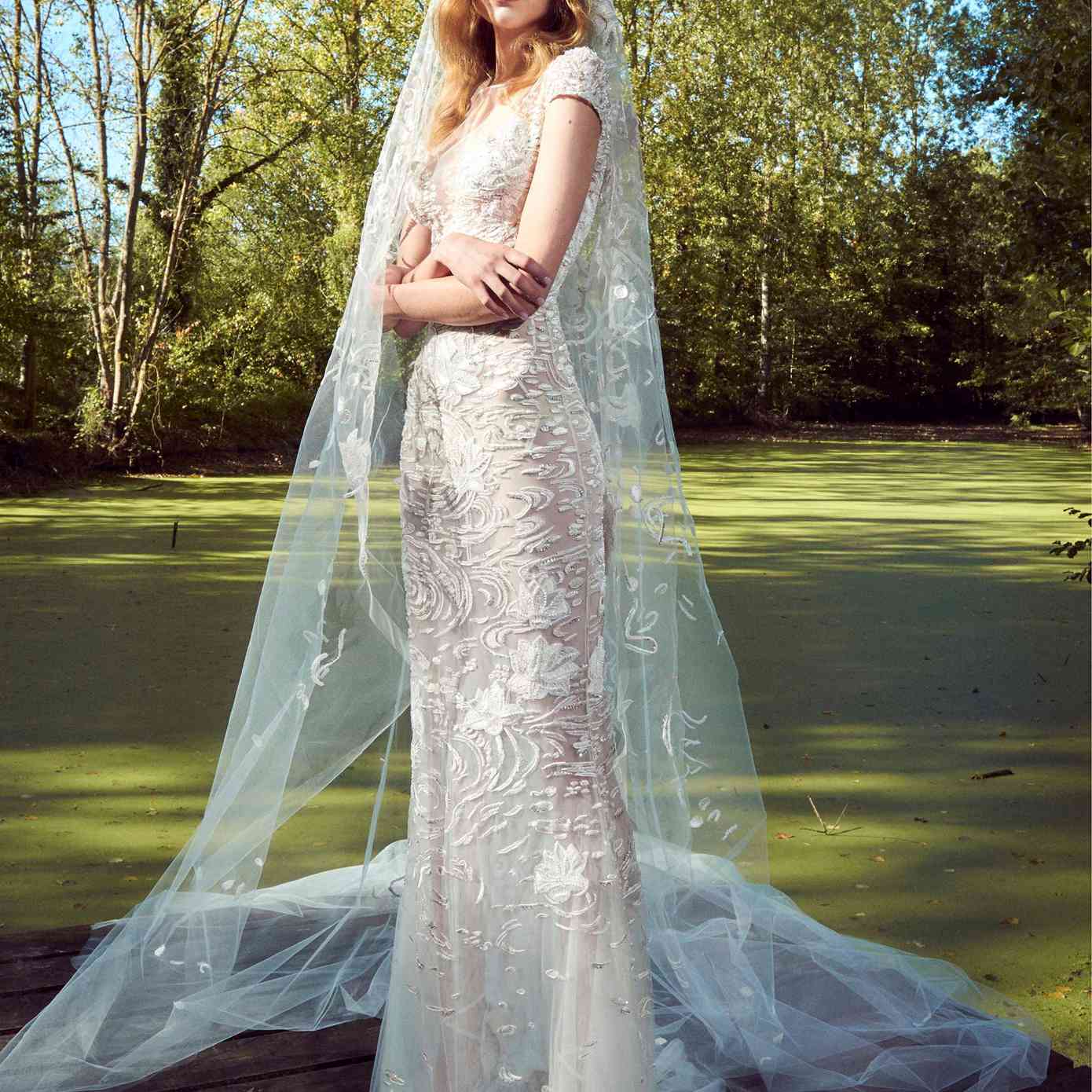 模型在薄纱鞘礼服帽袖,一个错觉领口,3 d串珠刺绣,和一个匹配的面纱