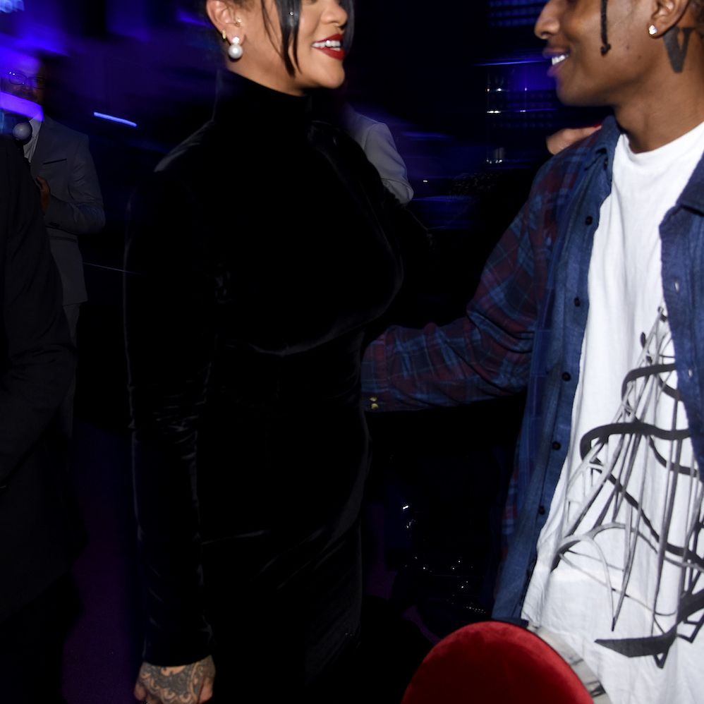 蕾哈娜身穿全黑套装，一只手搭在朋友a $AP Rocky的肩膀上，他抓住了她的腰。