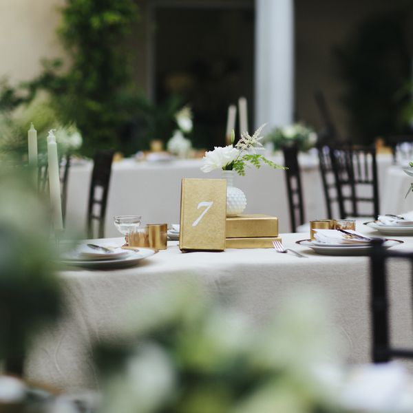 餐桌在一个室外结婚宴会/晚餐派对。表是完整的，带有第7号的地方设置，花卉安排和金色装饰。