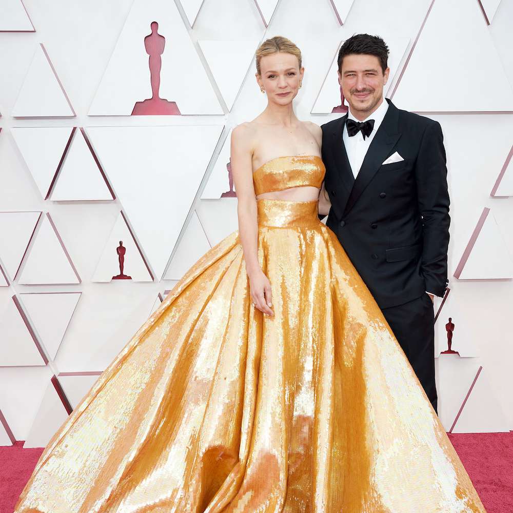 在2021年的奥斯卡红毯上，凯瑞·穆里根穿着一件金色的Valeninto胸罩和一条肥大的配套金色裙子站在丈夫马库斯·芒福德旁边