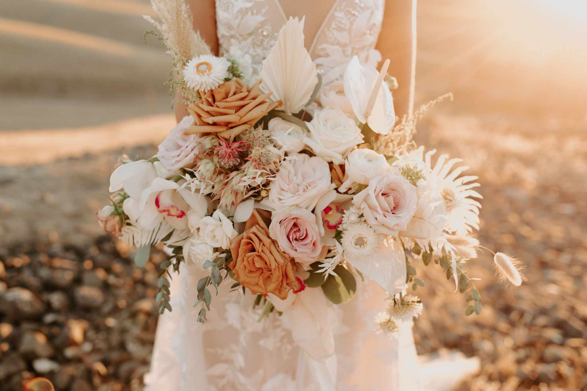 拿着白色，桃红色和棕褐色玫瑰的花束的新娘混杂与绿叶和蒲苇草枝