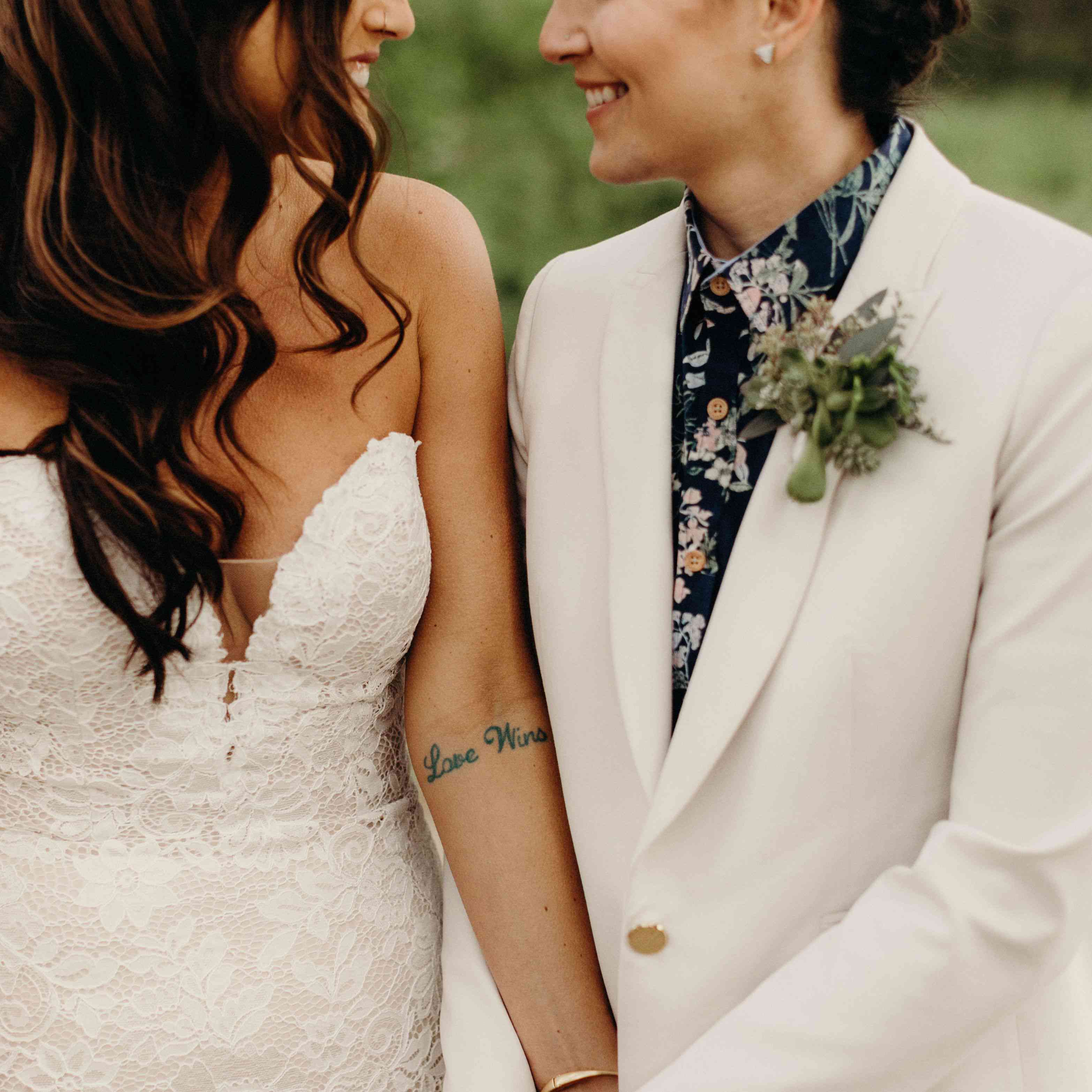 两个新娘微笑着牵手，有一个新娘的“爱胜利”纹身暴露