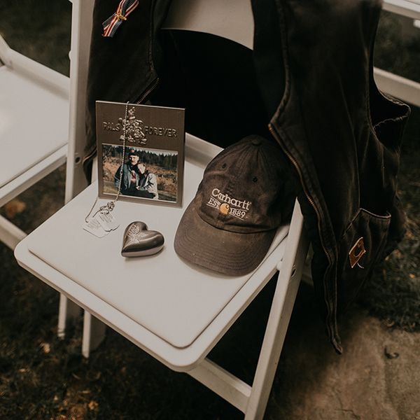 纪念新娘已故祖父的仪式椅，椅背上有一张照片，狗牌，一颗银色的心，卡哈特帽和卡哈特背心