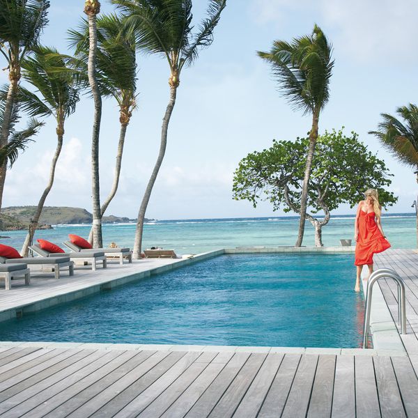 一名女子将她的脚浸在有棕榈树的海边游泳池里