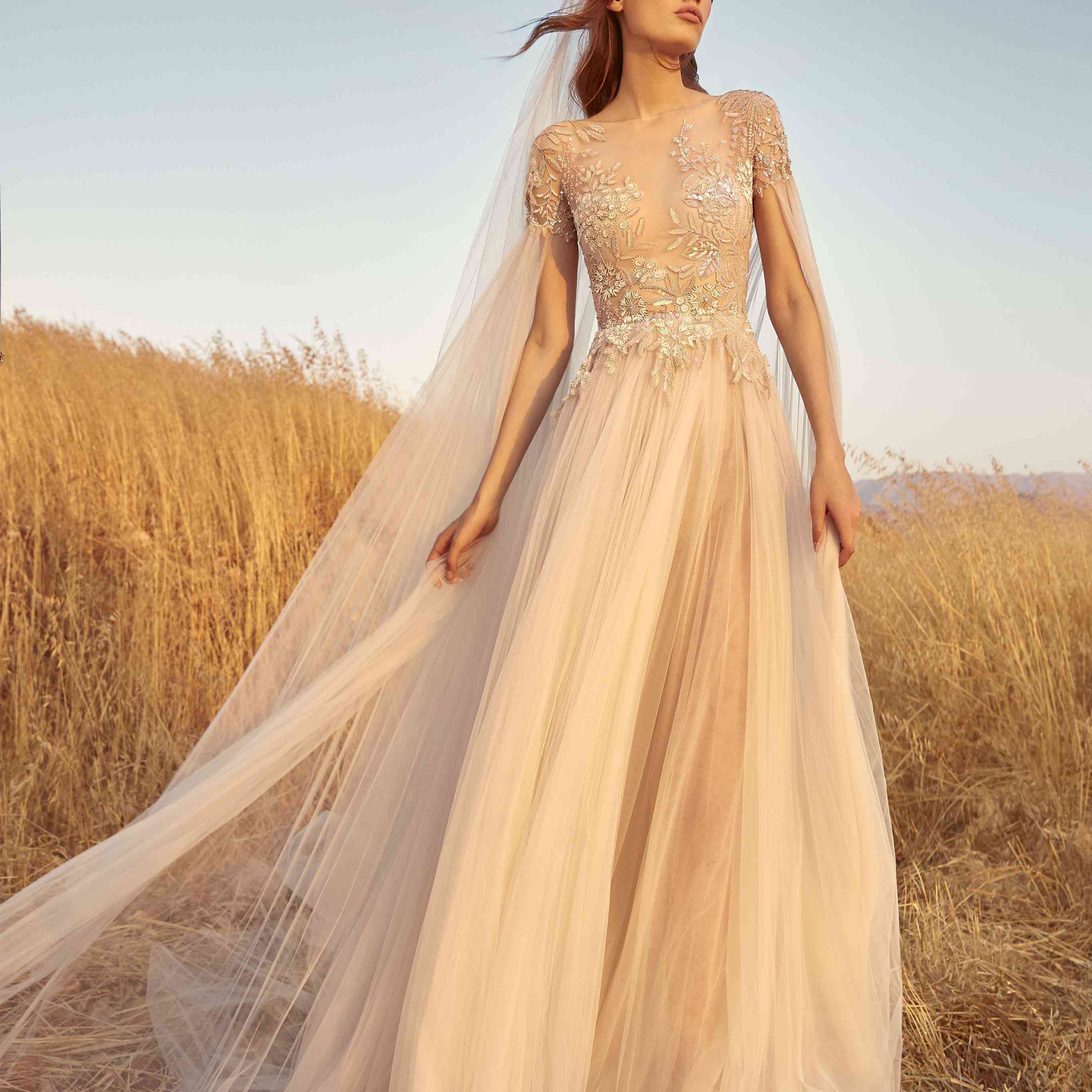 模型在喇叭,打褶的海胆薄纱衣服绣花上衣和戏剧性的长褶cape-like薄纱袖子和匹配的帽子