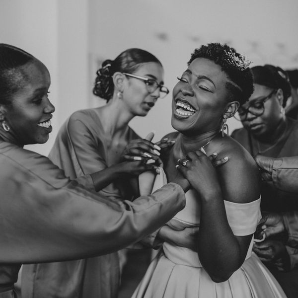 伴娘帮助微笑的新娘穿上礼服