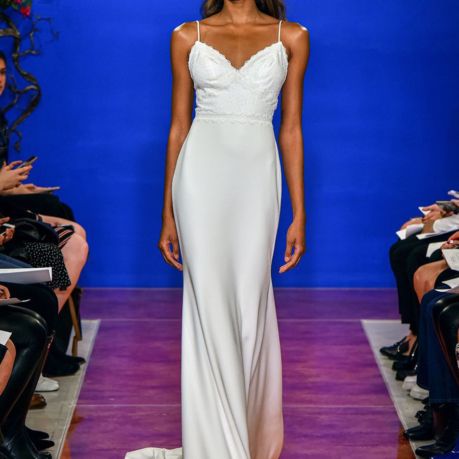 模型在意大利面条带V领柱式衣服的模型走下跑道，带蕾丝装饰