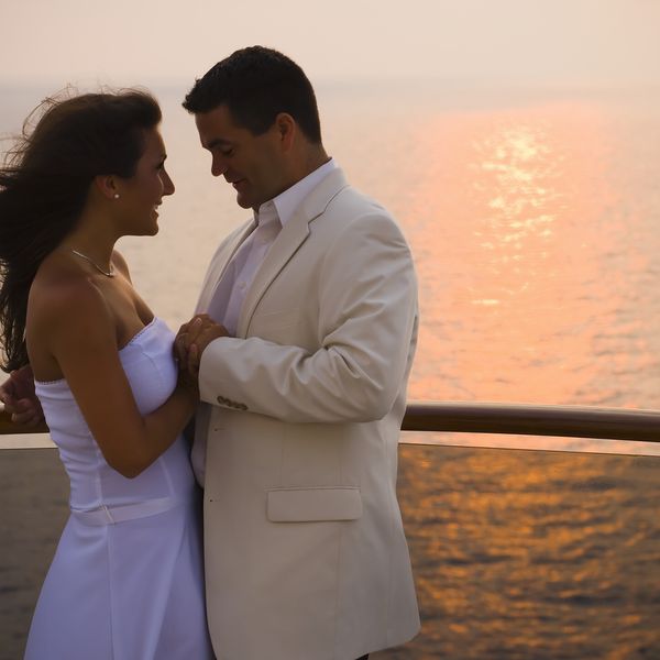 新娘和新郎手牵手在游轮甲板上，日落，侧面”class=