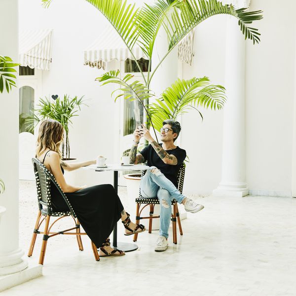 拍妻子照片的微笑的人与智能手机，当坐在室外咖啡馆时