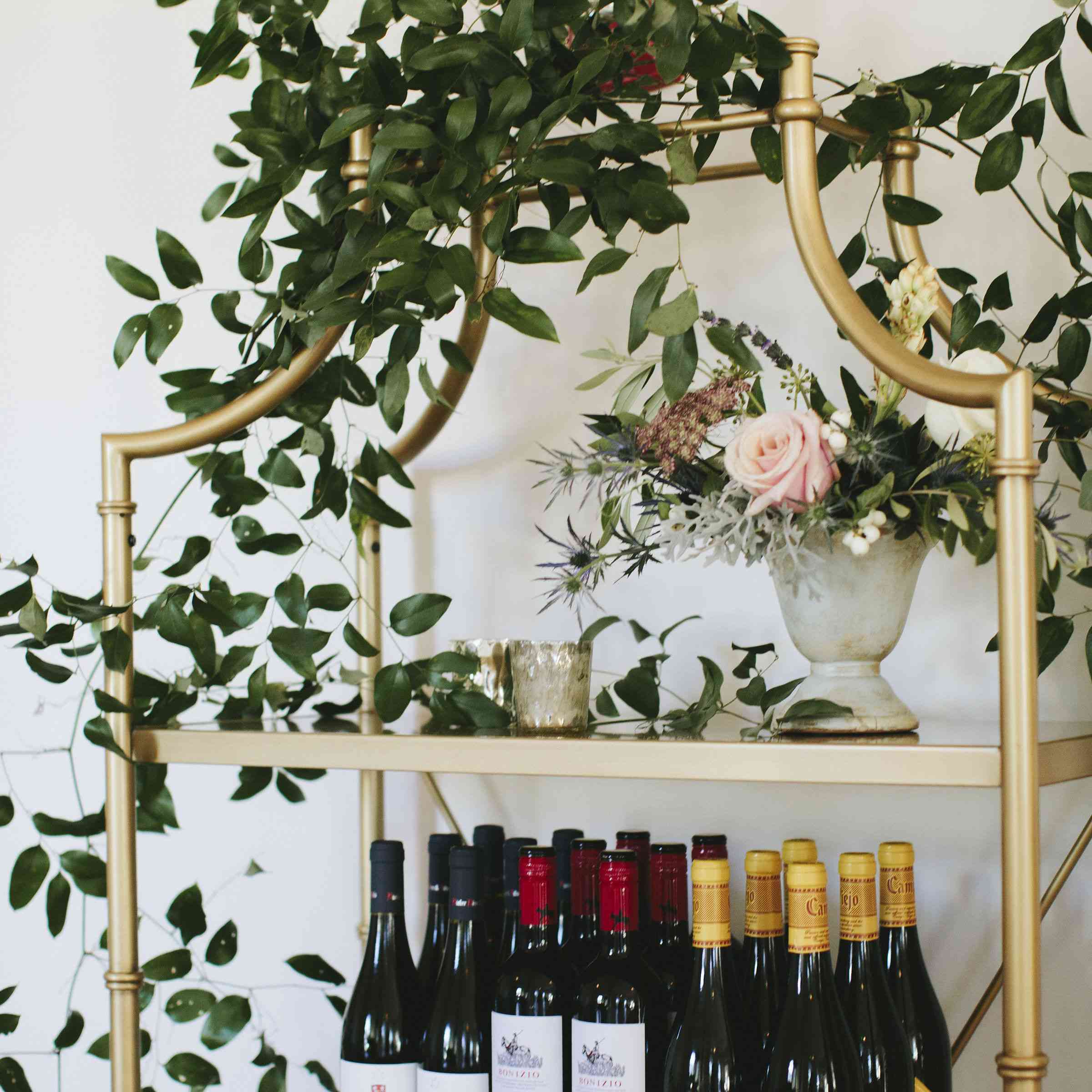 一瓶瓶的葡萄酒放在放着绿色植物的金丝架子上