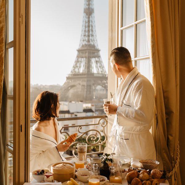 一对夫妇在酒店吃早餐，透过敞开的露台门眺望埃菲尔铁塔
